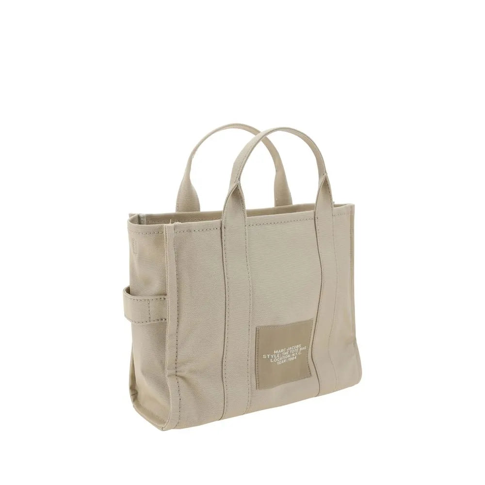 Beige cotton canvas Marc Jacobs Medium Tote bag with two tubular top handles, side strap loop, and front logo patch.