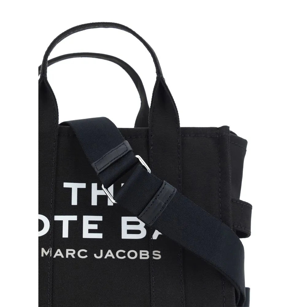 Black cotton Marc Jacobs small tote bag featuring white "THE TOTE BAG" logo, rigid top handles, and adjustable shoulder strap.
