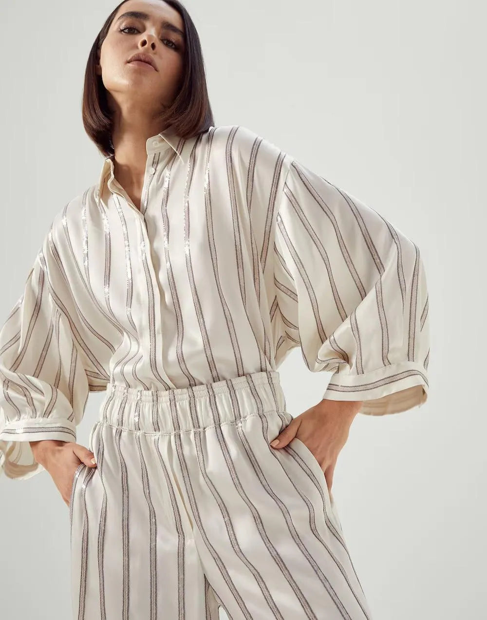 Brunello Cucinelli warm white acetate silk striped pants with elastic waist, paired with matching blouse.