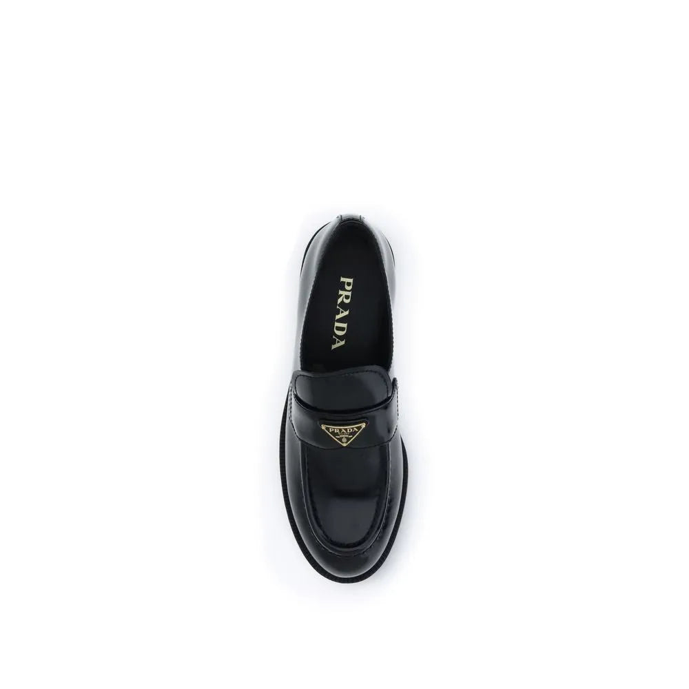 Black glossy calf leather Prada slip-on loafer with gold triangle logo on saddle and rounded toe.