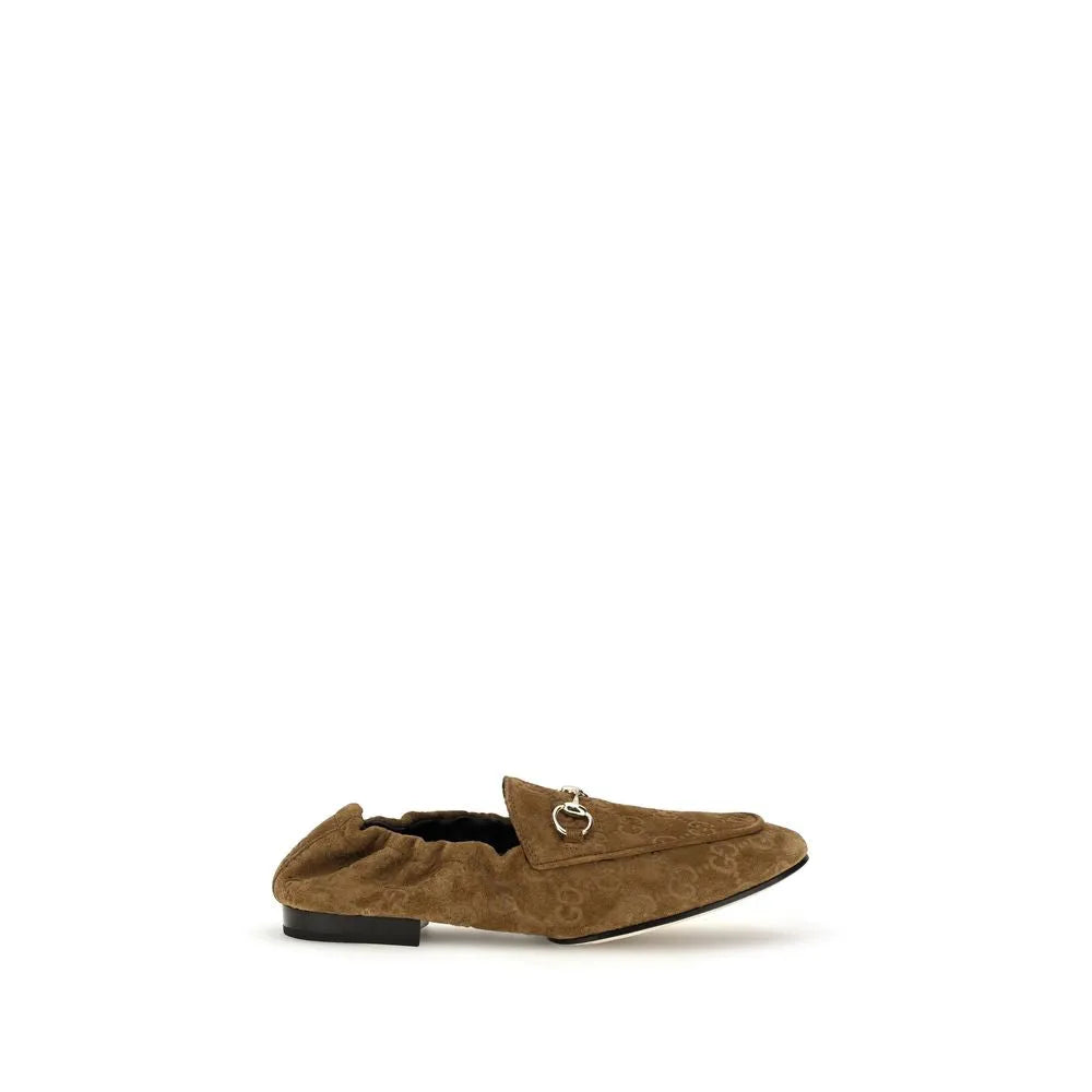 Brown Gucci suede slip-on loafers with embossed GG motif, metallic ring detail, and elasticized heel.