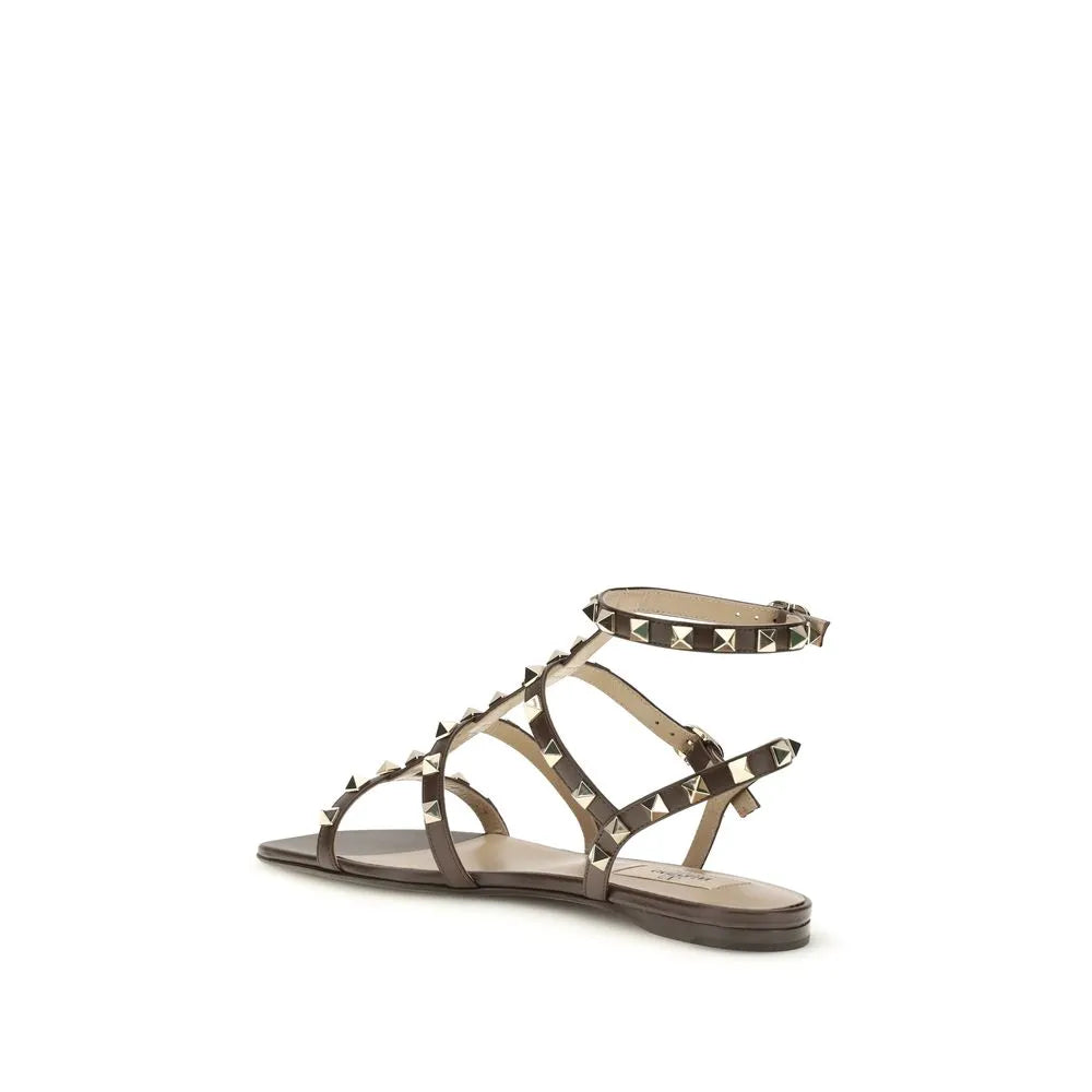 Brown calf leather flat sandals featuring Rockstud-style pyramid studs and an adjustable ankle strap.