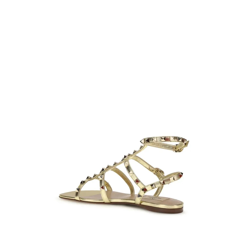 Gold laminated calf leather flat sandals with strappy design, platinum Rockstuds, and adjustable ankle strap.